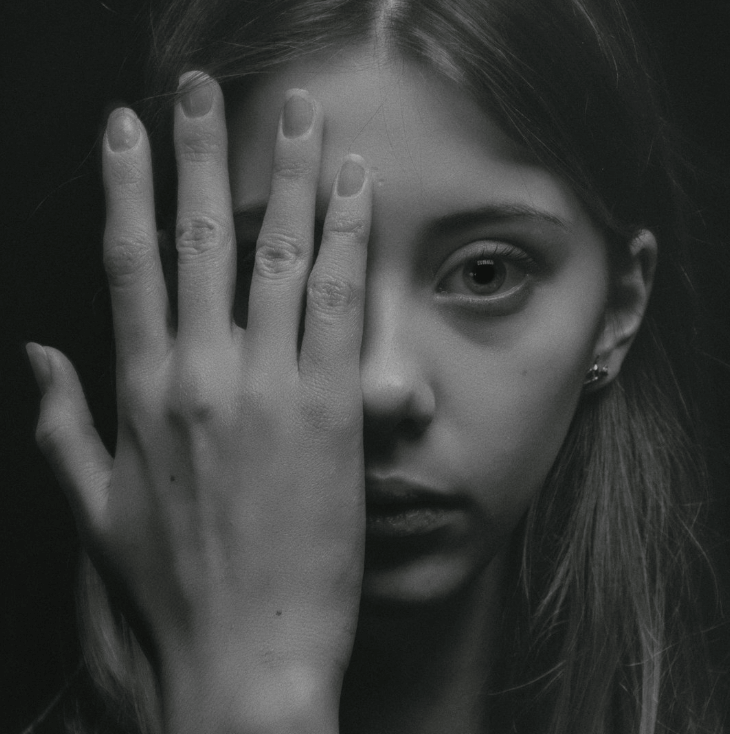 Black and white image of a young woman experiencing paranoid thoughts. She has large eyes, and her hand covers half of her face.