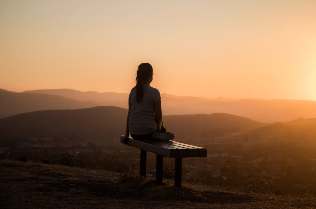 A woman sitting alone, relaxed and peaceful, watching the sunset and thinking about strategies for addressing anxiety in high-functioning autistic women.