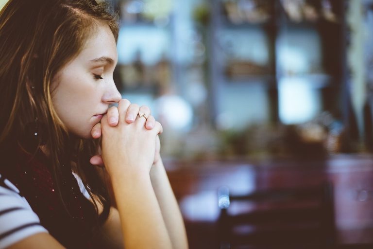 A woman with long brown hair is seen from the side. Her eyes are closed, and her hands are clasped near her face, symbolizing hope for mood stabilizer effectiveness in schizophrenia.